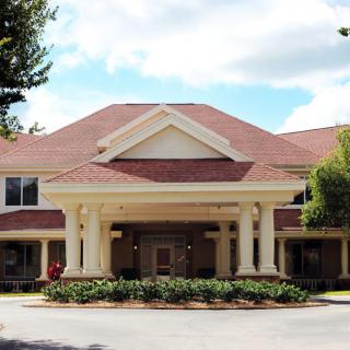A front view of a building with columns and a gabled roof, surrounded by landscaped greenery.