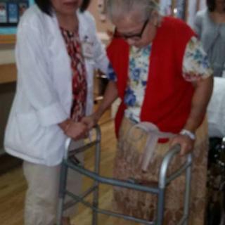 A healthcare worker assists an elderly person using a walker.