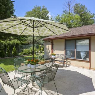 A sunny backyard patio with a glass table, chairs, and a large umbrella.