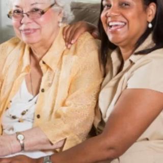 An elderly woman and her caregiver sitting together, smiling warmly at the camera.