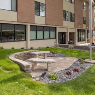A well-maintained outdoor seating area with stone benches and a garden, situated next to a building.
