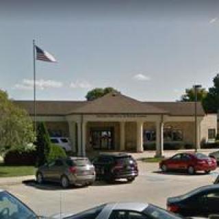 A building with an American flag flying, surrounded by parked cars and trees.