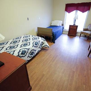 A simple bedroom with two beds, a chair, and a wooden floor.