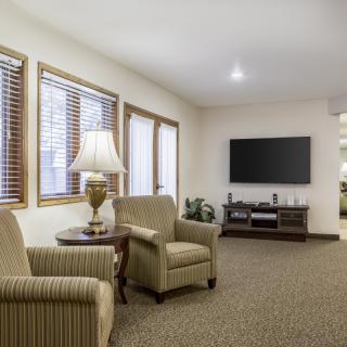 A cozy living room with armchairs, a lamp, and a wall-mounted television.