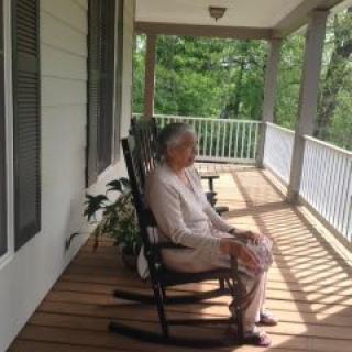 An elderly person sitting in a rocking chair on a porch, enjoying the outdoors.