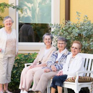 A group of senior women sitting on a bench outside, enjoying a sunny day.