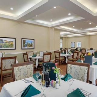 An elegantly set dining room with neatly arranged tables and chairs, featuring artwork on the walls.