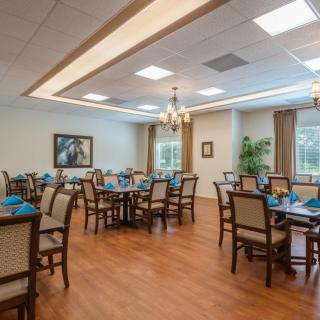 A well-lit dining room with neatly arranged tables and chairs, featuring wooden flooring and elegant lighting fixtures.
