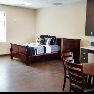A cozy bedroom setup featuring a comfortable bed, kitchenette, and dining area.
