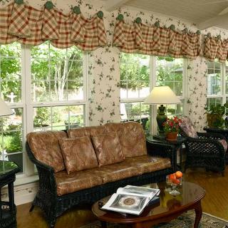 A cozy living room with floral wallpaper, featuring large windows, a patterned sofa, and a coffee table.