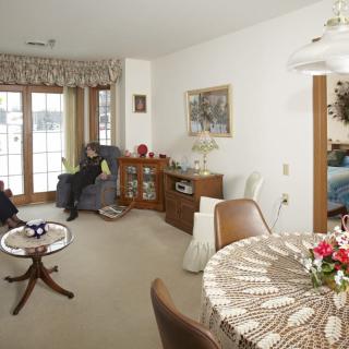 A cozy living room with a traditional interior design, featuring a dining table adorned with flowers and large windows letting in natural light.