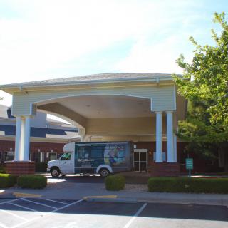 A building entrance with a van parked outside and trees in the background.