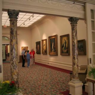 An interior view of an art gallery showcasing various paintings, with visitors admiring the artwork.