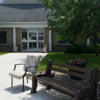 An outdoor seating area with a bench and chair in front of a building entrance.