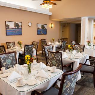 A neatly arranged dining area with several tables and chairs, featuring decorative table settings and floral centerpieces.