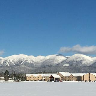 A snowy landscape with mountains in the background and buildings in the foreground under a clear blue sky.