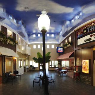 A charming indoor plaza with a sky-painted ceiling, featuring various shops and a central lamp post.