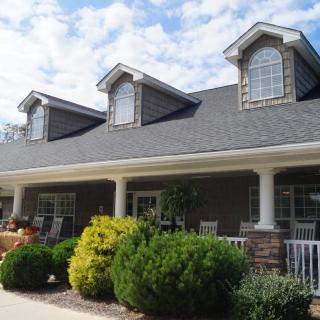 A suburban house with a sloped roof and front porch, surrounded by well-maintained landscaping.
