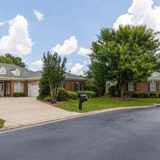 A suburban house with a driveway and surrounding trees under a partly cloudy sky.