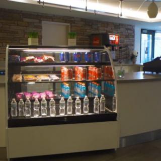 A cafe interior featuring a refrigerated display case filled with snacks and bottled water.