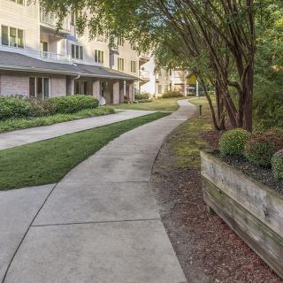 A curved sidewalk leads through landscaped greenery next to a residential building.