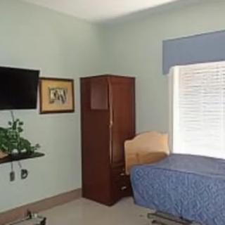 A simple bedroom with a bed, wardrobe, television, and a window with blinds.