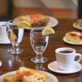 A breakfast table setting featuring coffee, water with lemon, and various dishes.