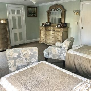 A cozy bedroom featuring a dresser with a mirror, upholstered chairs, and a table with lace covering.