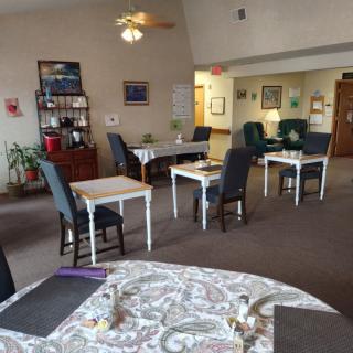 A cozy indoor dining area with neatly arranged tables and chairs, featuring a ceiling fan and warm decor.