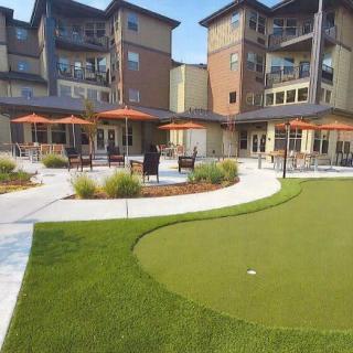Outdoor area with a putting green and seating in front of modern apartments.