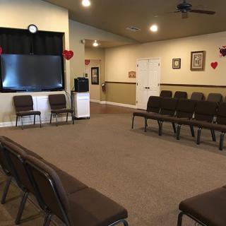 An indoor meeting room with chairs arranged in rows, a television and a projector screen at the front, and heart decorations on the walls.