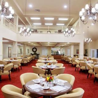 An elegant dining room with chandeliers, set with tables and chairs on a red carpet.