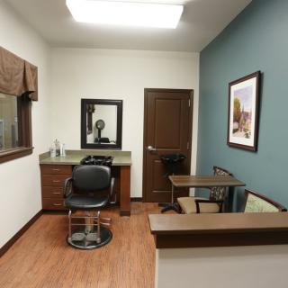A cozy hair salon room featuring a styling chair, mirror, and a small desk.