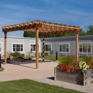 A serene outdoor area featuring a wooden pergola, flower beds, and modern architecture.