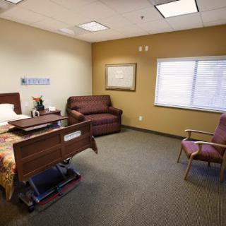 A spacious hospital room featuring a bed, seating areas, and natural light from the window.