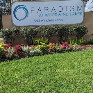 Entrance sign for Paradigm at Woodland Lakes, surrounded by vibrant landscaping.