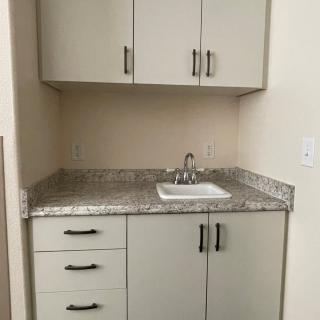 A small kitchen area with upper and lower cabinets, a countertop, and a sink.
