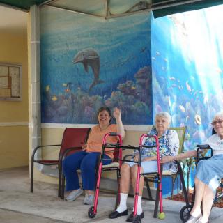 Three seniors sit together in front of a colorful aquatic mural, enjoying each other's company.