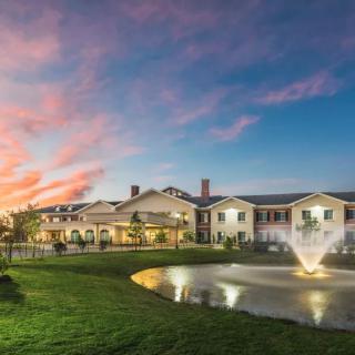 A picturesque view of a large building with a fountain and pond at sunset.