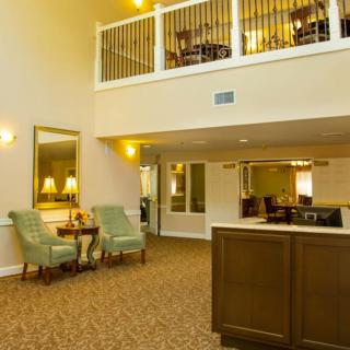 A well-lit lobby featuring a seating area with armchairs, a reception desk, and a two-story layout.