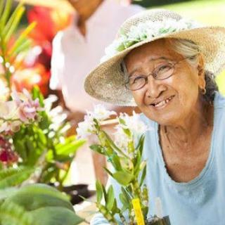 An elderly woman joyfully tending to her garden, surrounded by vibrant flowers.