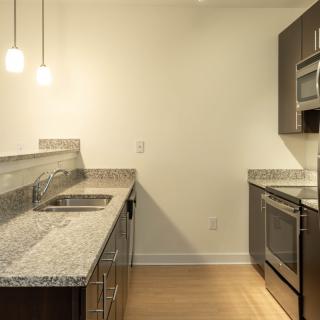 A modern kitchen with granite countertops, stainless steel appliances, and wood flooring.
