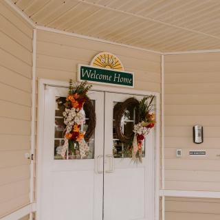 An entrance decorated with autumn-themed wreaths and a 'Welcome Home' sign.