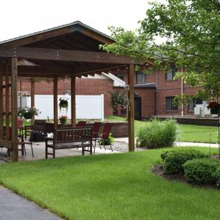 A tranquil garden featuring a wooden gazebo with benches, surrounded by a well-maintained lawn and landscaping.
