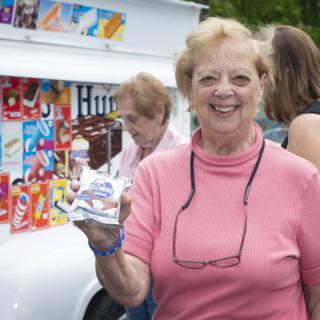 A woman in a pink shirt smiling while holding an ice cream cone in front of an ice cream truck.