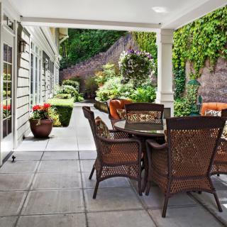 A cozy patio with a dining table and wicker chairs surrounded by lush greenery.