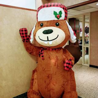 A person in a cheerful bear costume with holiday decorations stands indoors.