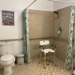 An accessible bathroom with a shower chair, grab bars, and a tiled floor for safety.
