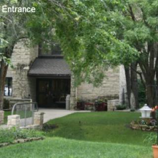A stone building entrance surrounded by trees and a well-maintained garden.