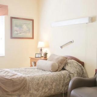 A cozy bedroom with a bed, lamp, chair, and artwork on the wall.
